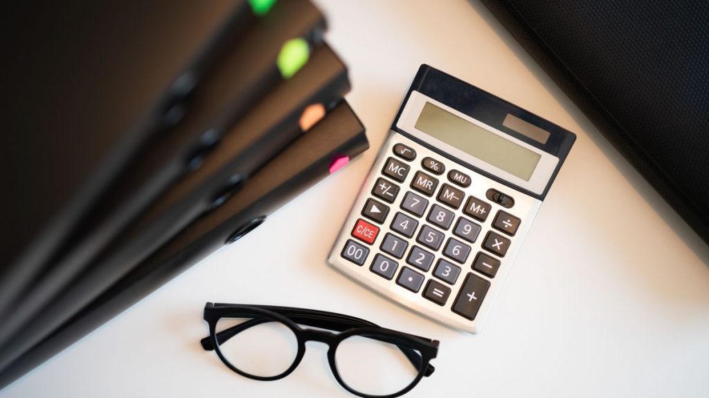 Calculatrice, lunettes et dossiers posés sur un bureau pour le calcul des frais de notaire